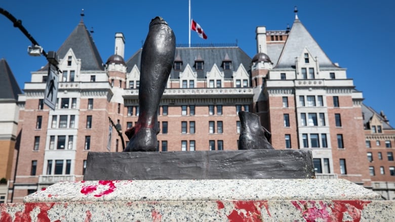 A metal sculpture of a dismembered leg and boot, with a historic building and a Canadian flag in the background.