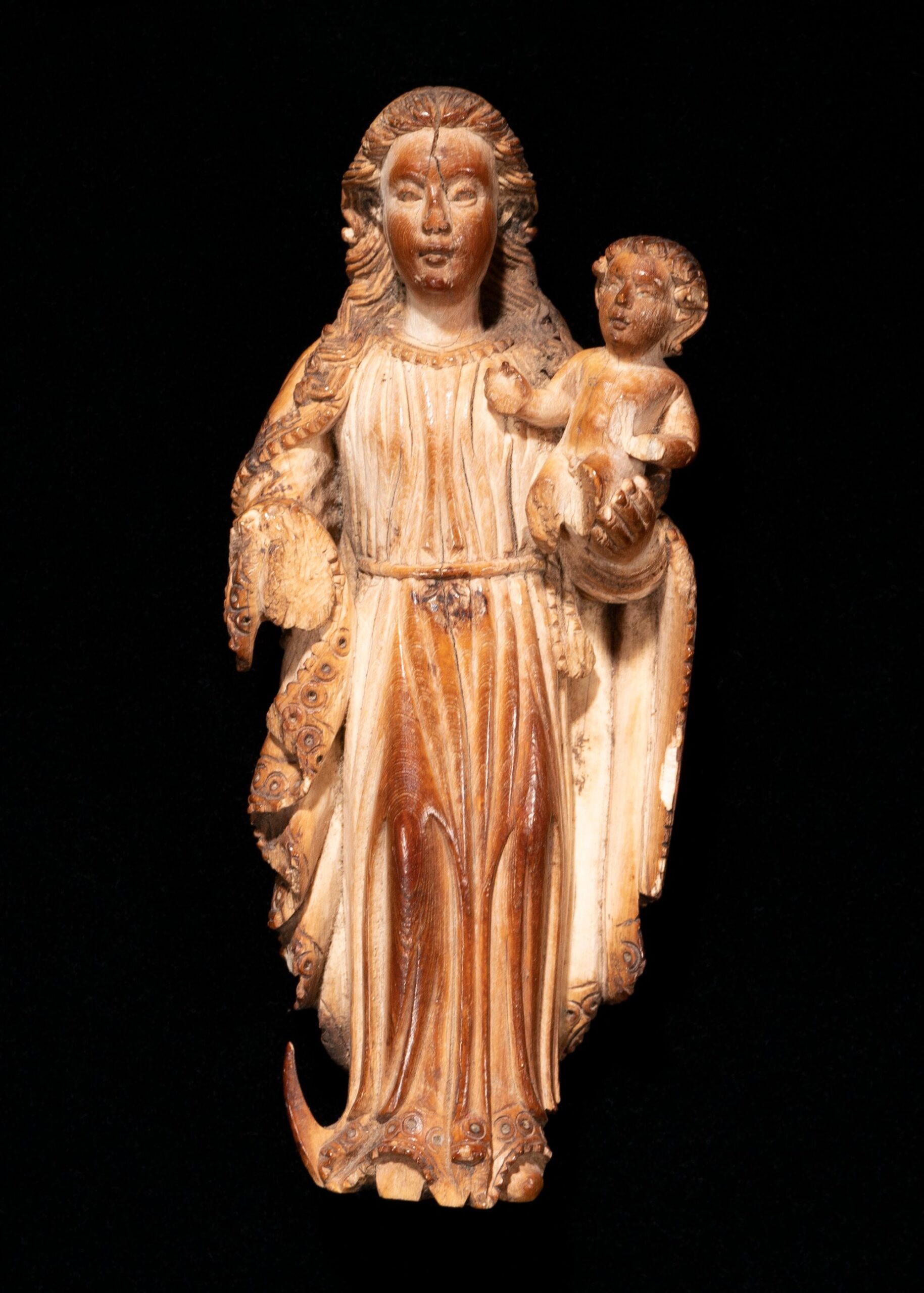 A carved figurine depicting a woman holding a child, detailed with intricate lines and textures, set against a black background.
