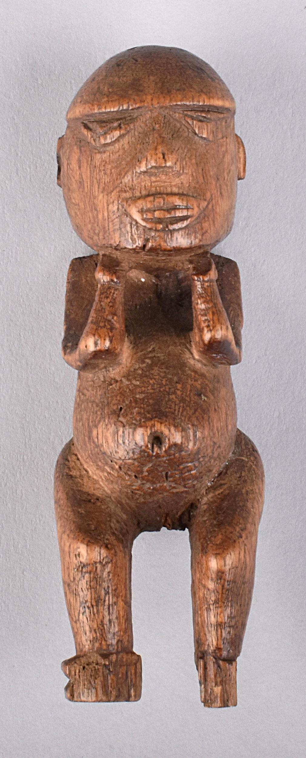 A carved wooden stylized human figure, with emphasis on round body shape and distinct limbs, set against a gray backdrop.