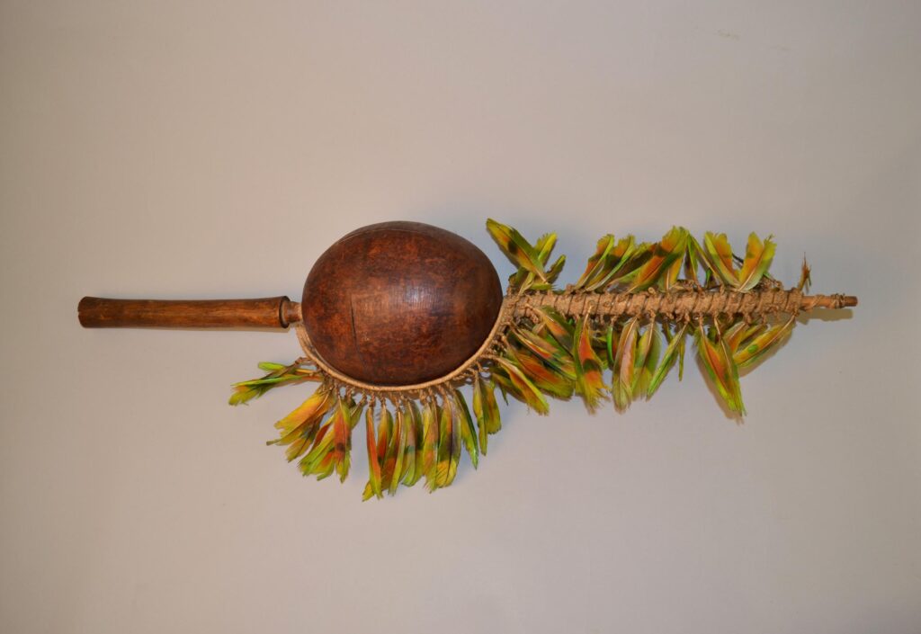 An artistic wooden instrument featuring a rounded body and a handle adorned with colorful feather embellishments.