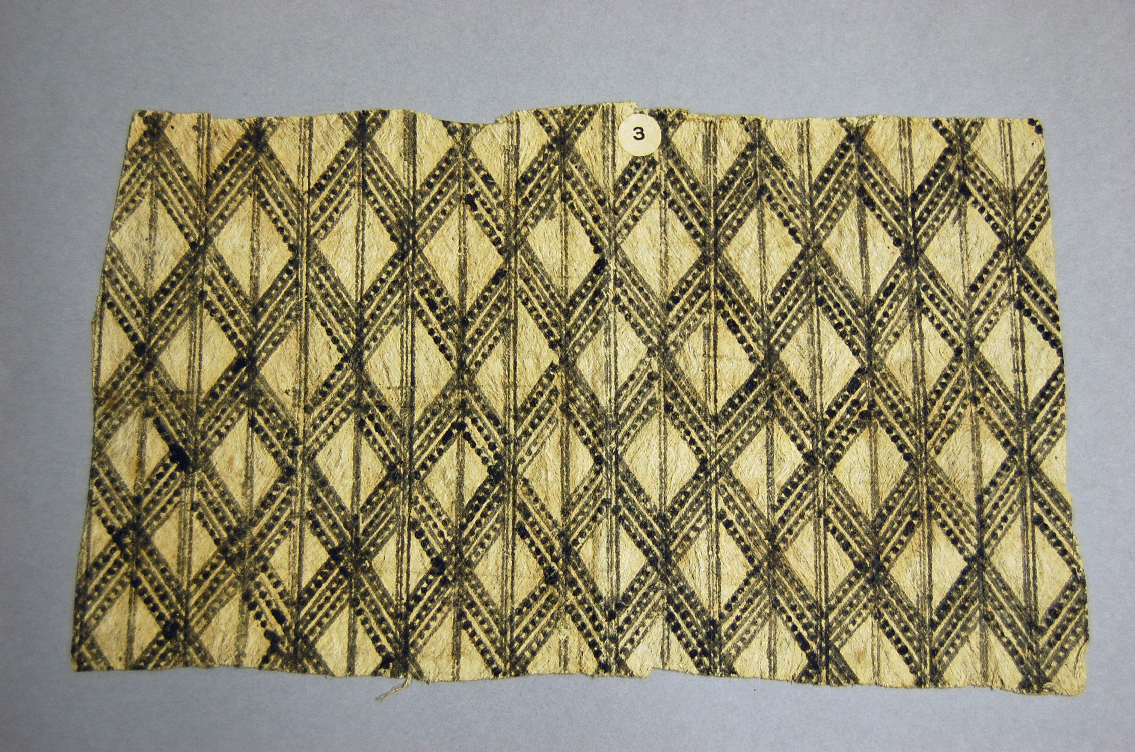 A textured fabric featuring interwoven diamond patterns in black and beige, labeled with a small white tag marked 3.