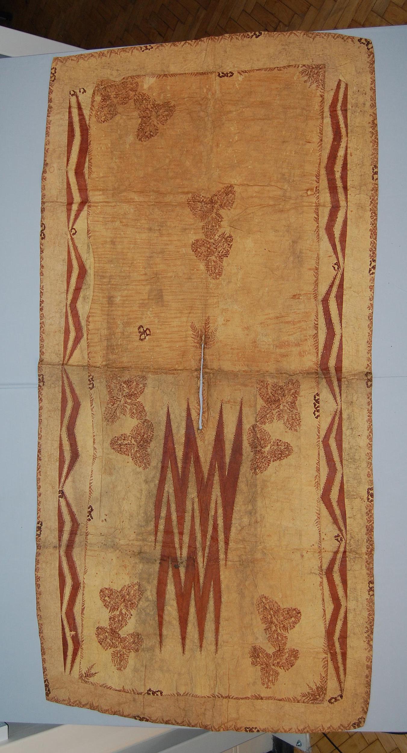 Textile featuring intricate red patterns on a beige background, showcasing floral and zigzag designs.