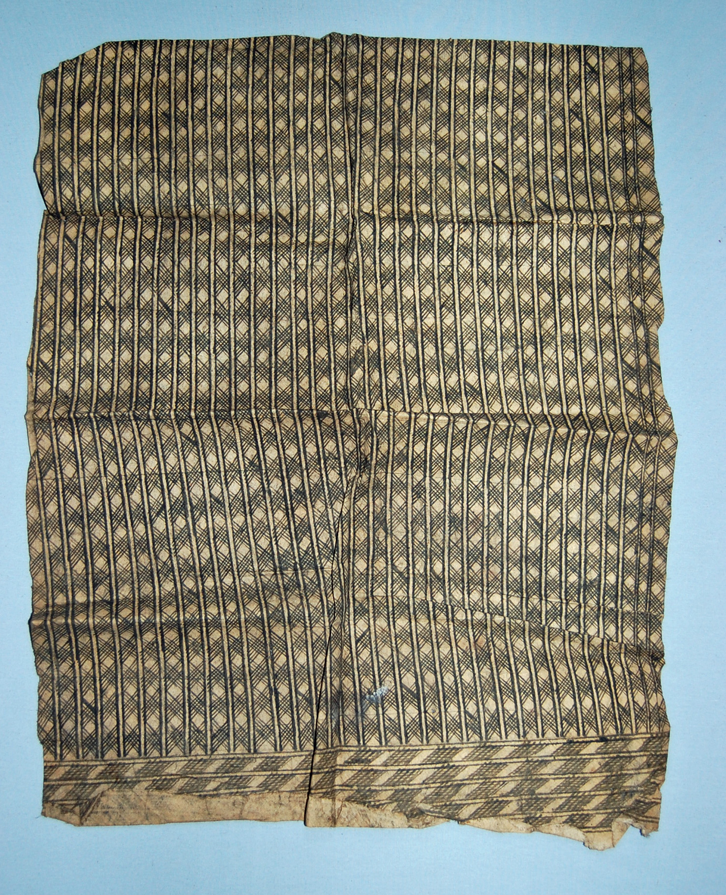 Close-up of a textile showcasing intricate black and beige geometric patterns, with minor wear and fraying along the edges.