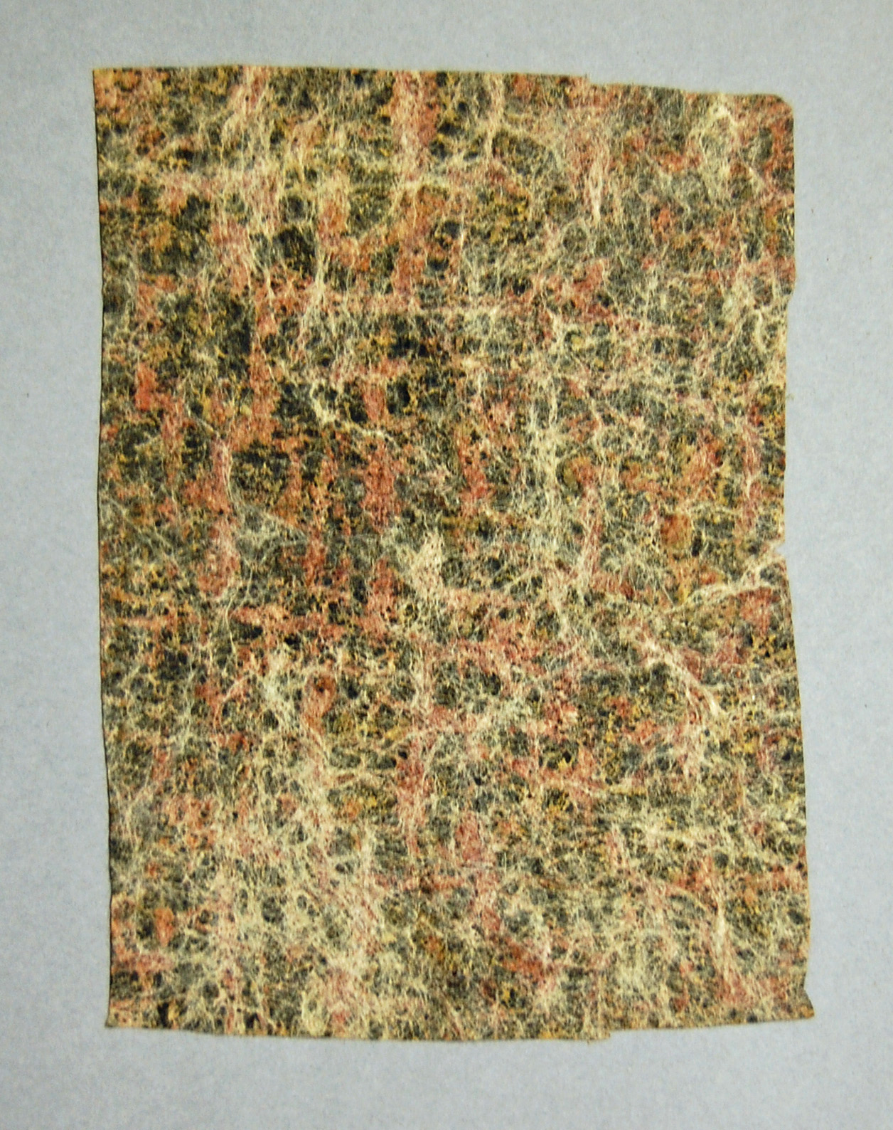 A textured piece of barkcloth with a mottled pattern in shades of black, orange, and cream, resembling natural stone.
