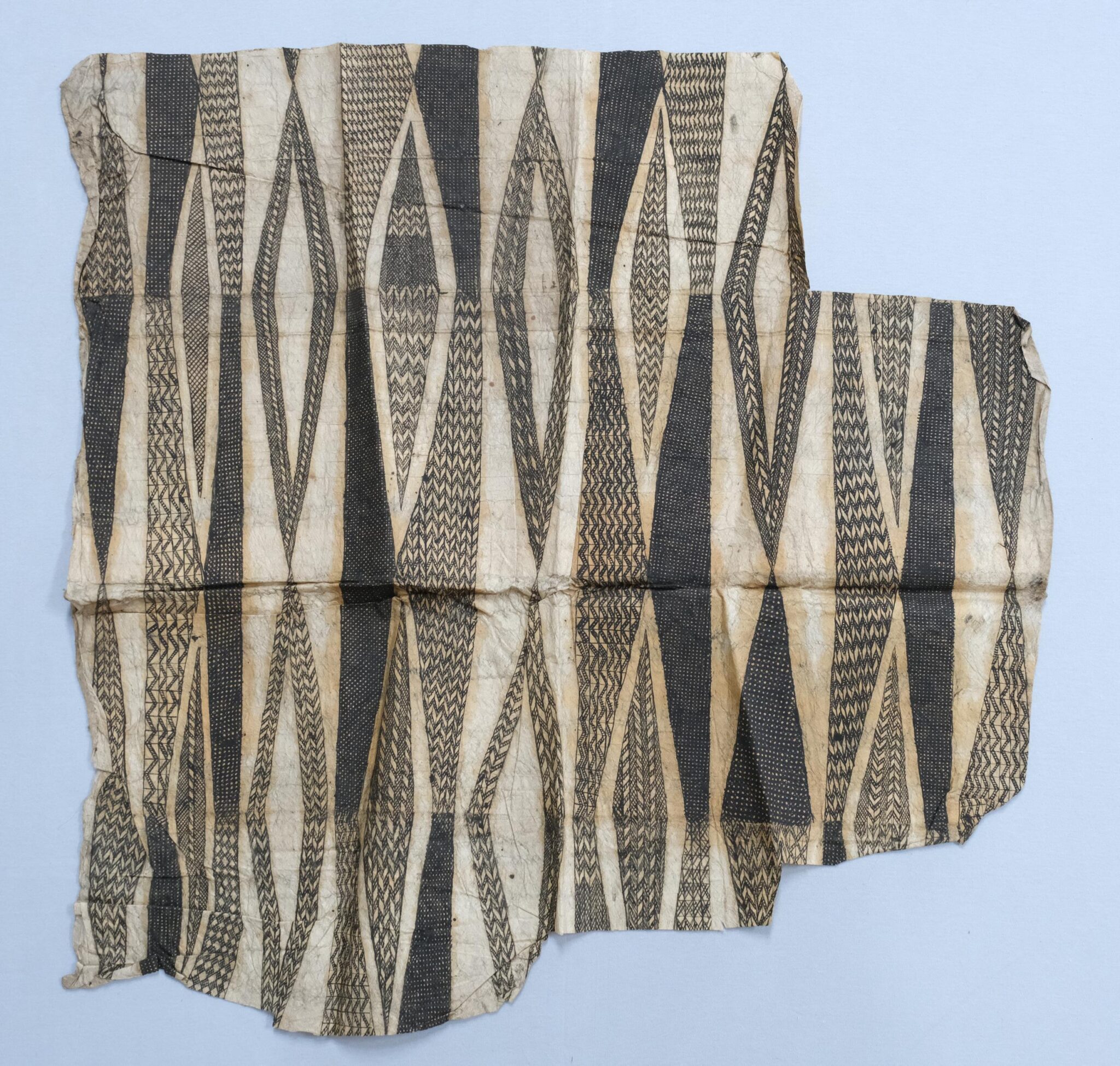 A fragment of patterned fabric featuring elongated diamond shapes and intricate black and beige designs, showcasing textile artistry.