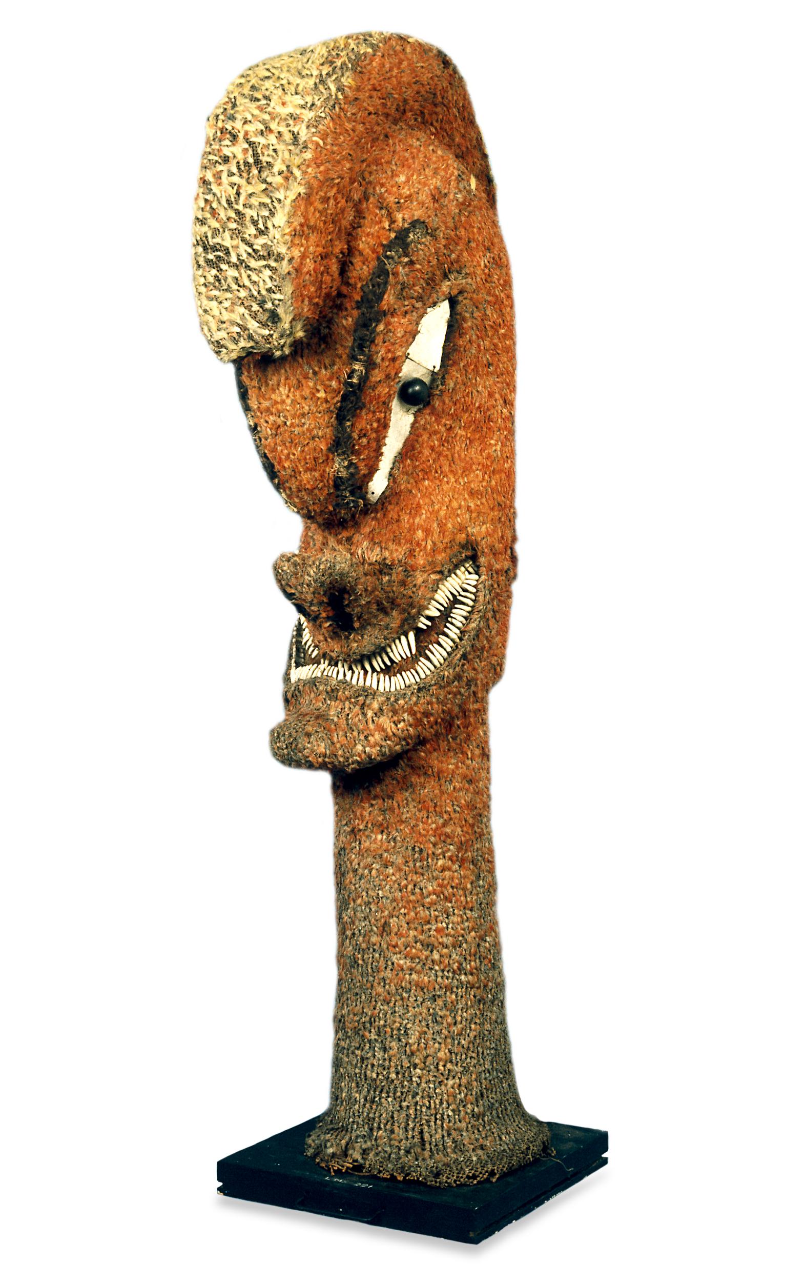 A stylized, tall wooden sculpture of a face with exaggerated features, adorned with textured fabric and shells.