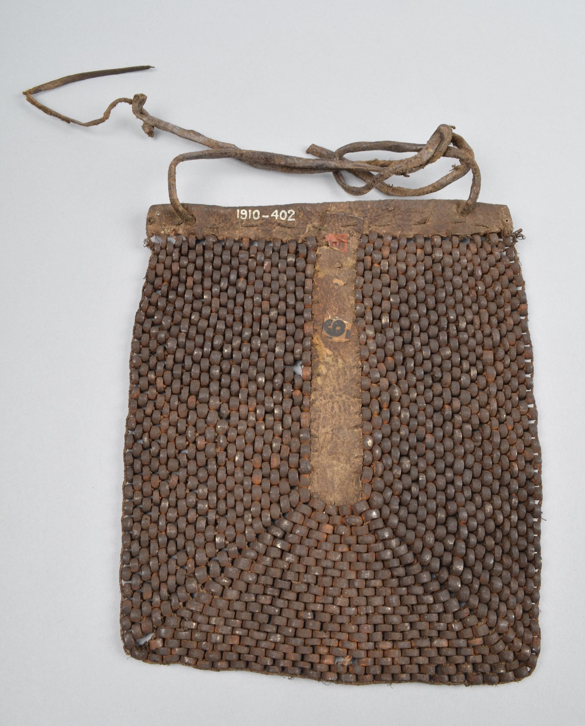 A handmade woven bag with a wooden top bar and a leather strap, featuring a textured pattern of small, dark beads.
