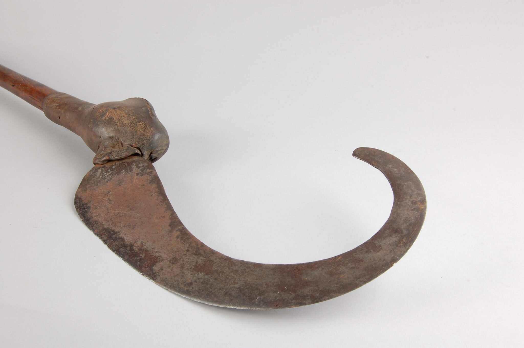 Close-up of an antique, rusted hook on a wooden handle, resembling a traditional farming or harvesting tool.