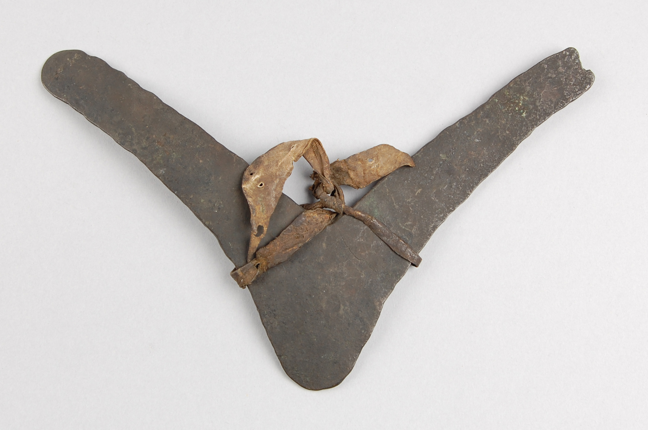 A vintage metal artifact shaped like a 'V', featuring a twisted fabric and leather binding at the center.