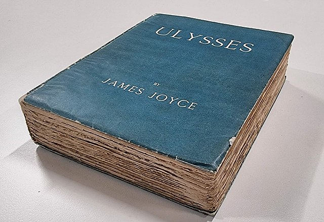 A worn copy of Ulysses by James Joyce, featuring a blue cover with white lettering, resting on a flat surface.